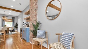A modern kitchen with wooden cabinets, a brick accent wall, and a round mirror. - Walk 2 Beach-Hot Tub-2 King beds-Waffle bar-Bikes (Galveston)