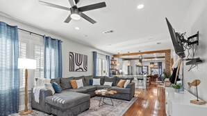 A modern living room with a sectional sofa, a coffee table, and a flat-screen TV mounted on the wall. - Walk 2 Beach-Hot Tub-2 King beds-Waffle bar-Bikes (Galveston)