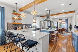 Una cocina moderna con una isla central, taburetes de bar, iluminación colgante y vigas de madera.