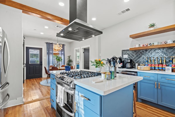 Une cuisine moderne avec des meubles bleus, un îlot central, des appareils en acier inoxydable et un dosseret de carrelage disposé en motif chevron.
