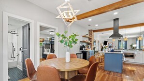 A modern kitchen with a central island, wooden flooring, and a dining area with a round table and chairs. - Walk 2 Beach-Hot Tub-2 King beds-Waffle bar-Bikes (Galveston)