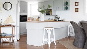 Una cocina moderna con armarios blancos, una isla central con taburetes y un comedor con mesa y sillas de madera.