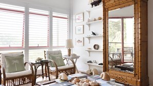 Una habitación con muebles de mimbre, un espejo grande y varios objetos decorativos como conchas marinas y libros.