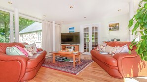 Ein Wohnzimmer mit zwei Ledersofas, einem Couchtisch, einem Fernseher und einem großen Fenster mit Vorhängen.