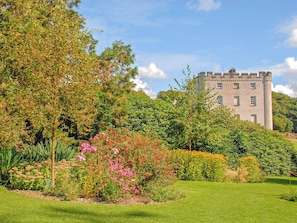 Een kasteel omringd door weelderige begroeiing en een verzorgde tuin.