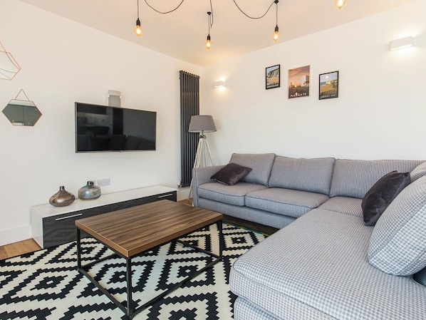 Una sala de estar moderna con un televisor de pantalla plana grande, una alfombra estampada, un sofá y una mesa de centro.