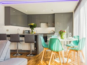Una cocina moderna con armarios grises, una isla central con taburetes de bar y un comedor con mesa redonda y sillas verdes.