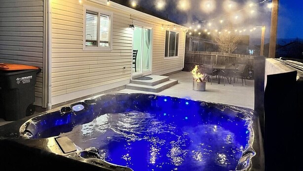 A hot tub with string lights, a patio with chairs, and a house with a door and windows. - Colorado Springs Home · Hot Tub · Built for Longer Stays (Colorado Springs)