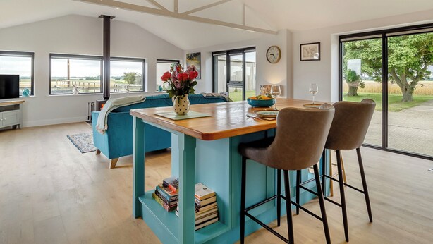 A spacious living area with a dining table, bar stools, a sofa, and a TV.