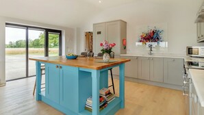 A kitchen with a blue island, a dining area with a table and chairs, and a view of a field through a glass door.