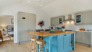 A modern kitchen with a central island, bar stools, and a dining area with a bed and a chair.