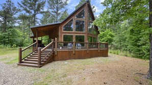 A cabin with a wooden exterior, large windows, and a covered porch with stairs. - Great Views, High Speed Internet, Hot Tub, Fireplace, Balcony, Sauna, Loft! (Broken Bow)