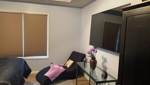 Un dormitorio con una cama, una mesita de vidrio con un florero y una silla, además de un espejo grande.