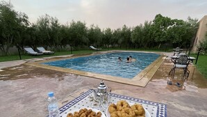 A poolside table with plates of fried dough, a water bottle, and a teapot. - Dar izniren (Ourika)