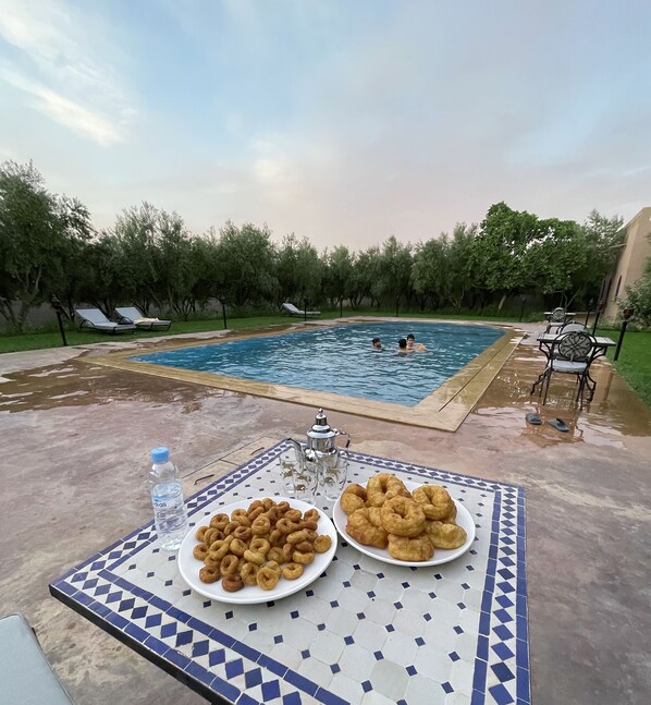A poolside table with plates of fried dough, a water bottle, and a teapot.