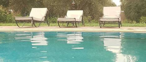 Relax by the serene pool surrounded by lush greenery and shaded lounge chairs.