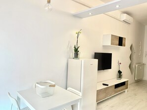 A modern living room with a white TV stand, a flat-screen TV, a small table with a basket, and a potted plant. - Sunset suite - apartment by the sea in Marina di Carrara (Marina di Carrara)