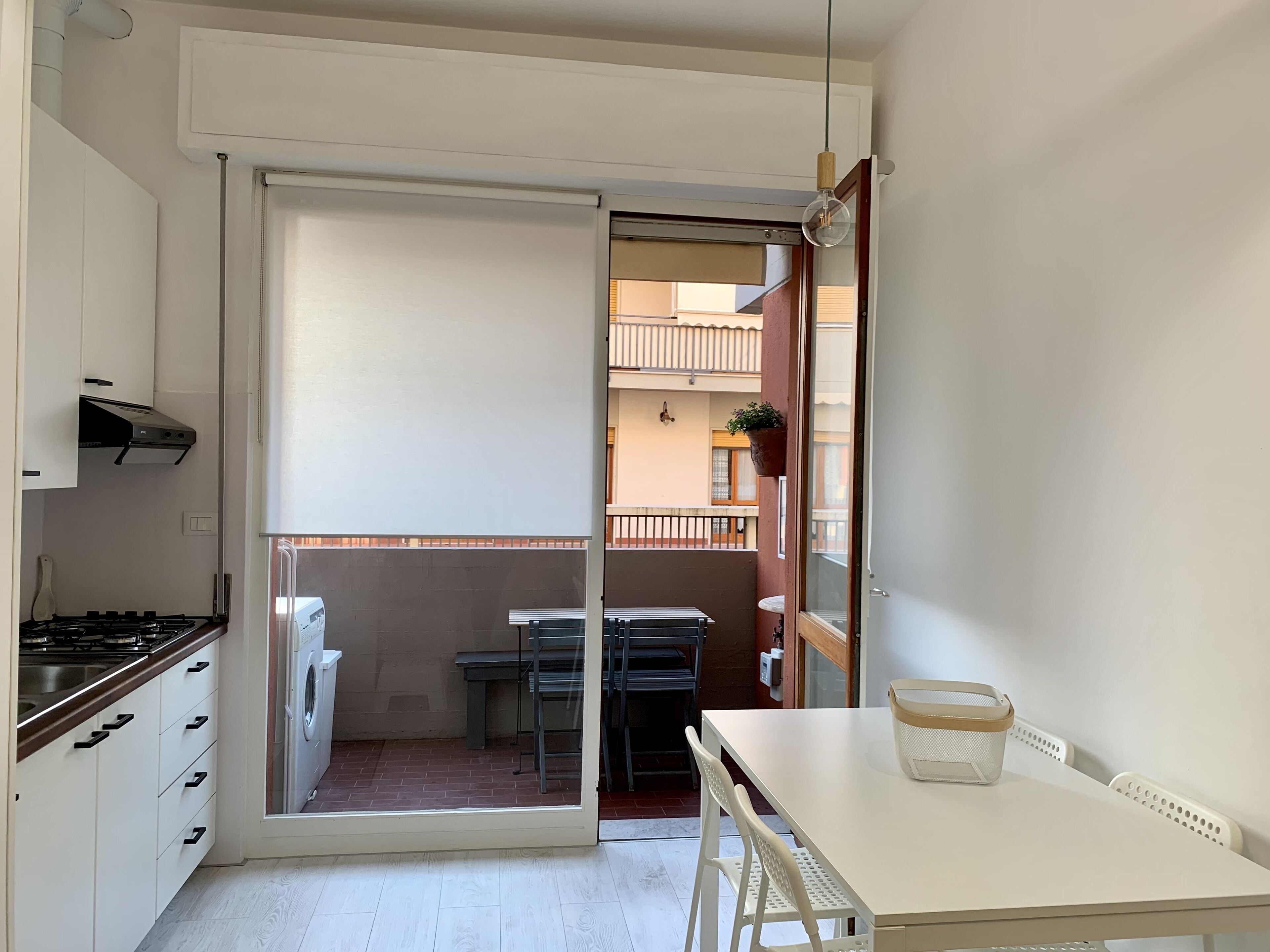 A compact kitchen with a gas stove, a washing machine, and a sliding glass door leading to a balcony with a table and chairs.