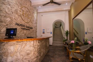 A hotel reception area with a stone wall, a reception desk, a computer, and a staircase leading to the upper floors.