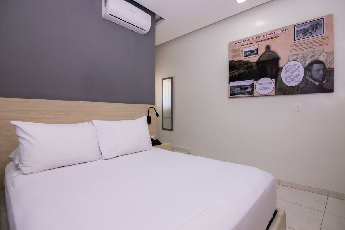 Una habitación de hotel con una cama, aire acondicionado de pared y un cartel en la pared.