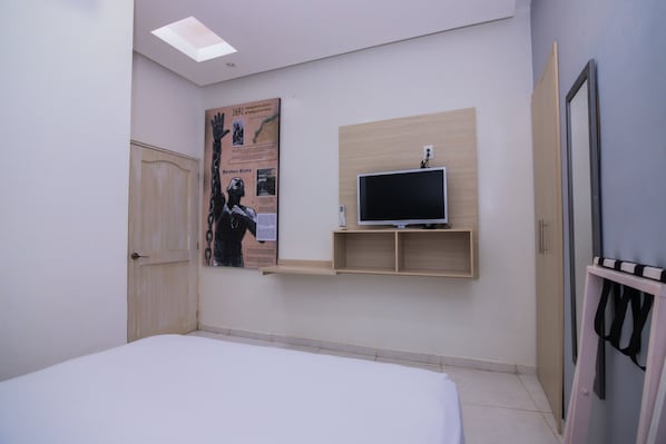 A bedroom with a bed, a mounted TV, a wooden shelf, a door, and a poster on the wall.