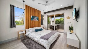Ein modernes Schlafzimmer mit einem großen Bett, einem Schreibtisch, einem Fernseher und einem Balkon mit Sitzgelegenheit.