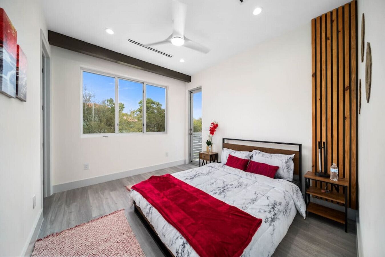 Un dormitorio moderno con una cama grande, un ventilador de techo y vistas a árboles por la ventana.