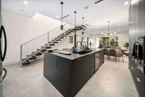 A modern kitchen with a central island, a staircase, and a dining area. - Luxury 3/4 Home in Las Olas with Pool and Hot Tub Near the Beach (Fort Lauderdale)
