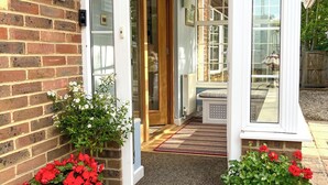 Une entrée de maison en briques avec une porte blanche, un petit porche et des plantes en pot.