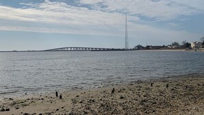 A beach with a pier extending into the water, a tall communication tower, and buildings in the background. - Perfect Hamptons Family Fall escape (Hampton Bays)