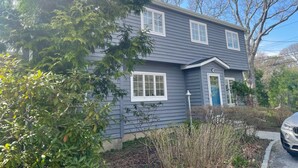 A two-story house with a gray exterior, white windows, and a blue door. - Perfect Hamptons Family Fall escape (Hampton Bays)