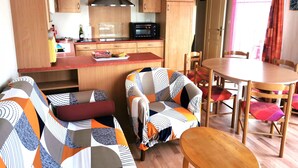 A compact living space with a kitchenette, a dining area, and a sofa with a colorful quilt. - Le Cocon des Dunes - Heated swimming pools (Brem-sur-Mer)