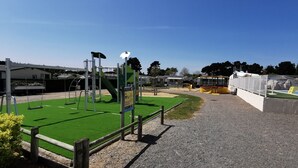 A playground with swings, a climbing structure, and a fenced area with a slide. - Le Cocon des Dunes - Heated swimming pools (Brem-sur-Mer)