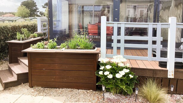 A wooden deck with a glass enclosure, a white fence, and a planter with plants. - Le Cocon des Dunes - Heated swimming pools (Brem-sur-Mer)