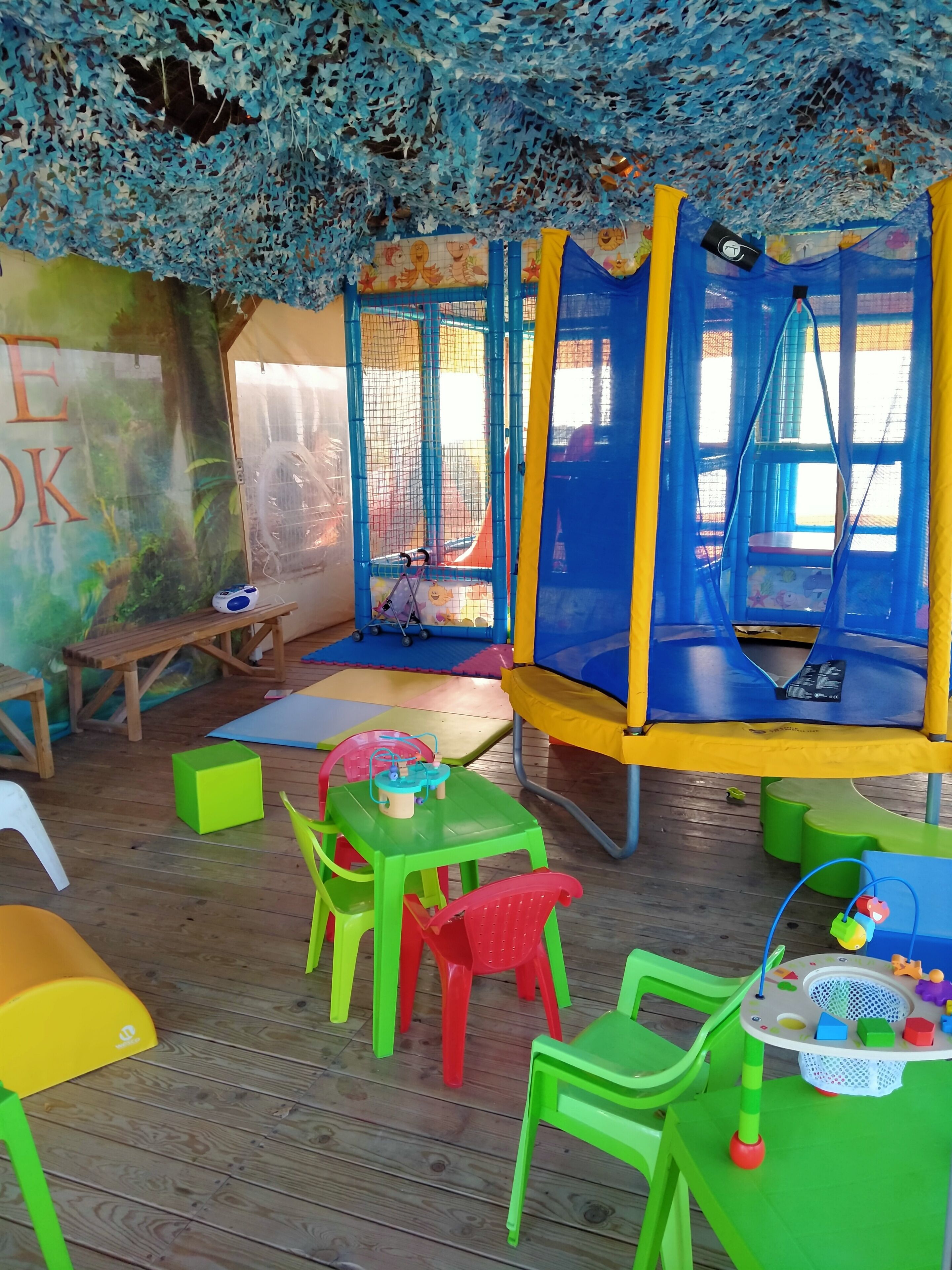 Zona de jocs infantil amb un trampolí, cadires colorades i una taula plena de joguines.