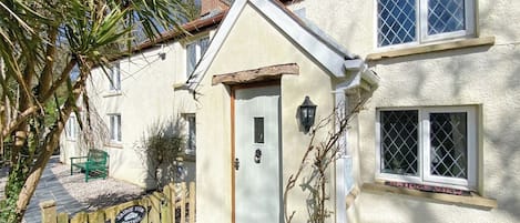 A house with a white exterior, a wooden door, a window with a lattice design, and a sign that reads 'BRIDGE VIEW COTAGE.'