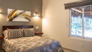 Een slaapkamer met een bed, een aan de muur hangend kunstwerk, een nachtkastje en een raam met uitzicht op groen.