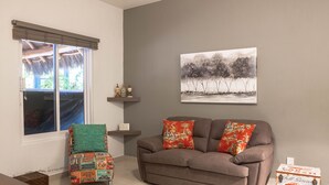 Een woonkamer met een bruine bank, een kleurrijke fauteuil en een schilderij aan de muur.