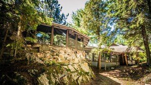 Une cabane rustique, avec des fondations en pierre, entourée d’une forêt dense.