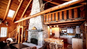 L’intérieur d’un chalet rustique, avec une cheminée en pierre, des meubles en bois et un coin cuisine.