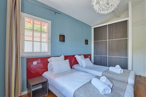 A hotel room with two beds, a window with a view, a small bedside table, and a decorative ceiling light.