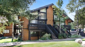 A modern two-story house with a wooden exterior, large windows, and a black staircase leading to a balcony.
