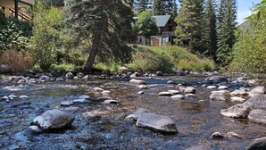 A river with rocks, surrounded by trees and a building with a porch.
