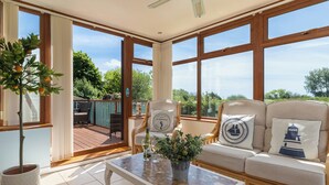 Ein sonnendurchfluteter Raum mit einer Glastür, die auf eine Außenterrasse führt, ein Sofa mit nautisch inspirierten Kissen und einem Deckenventilator.