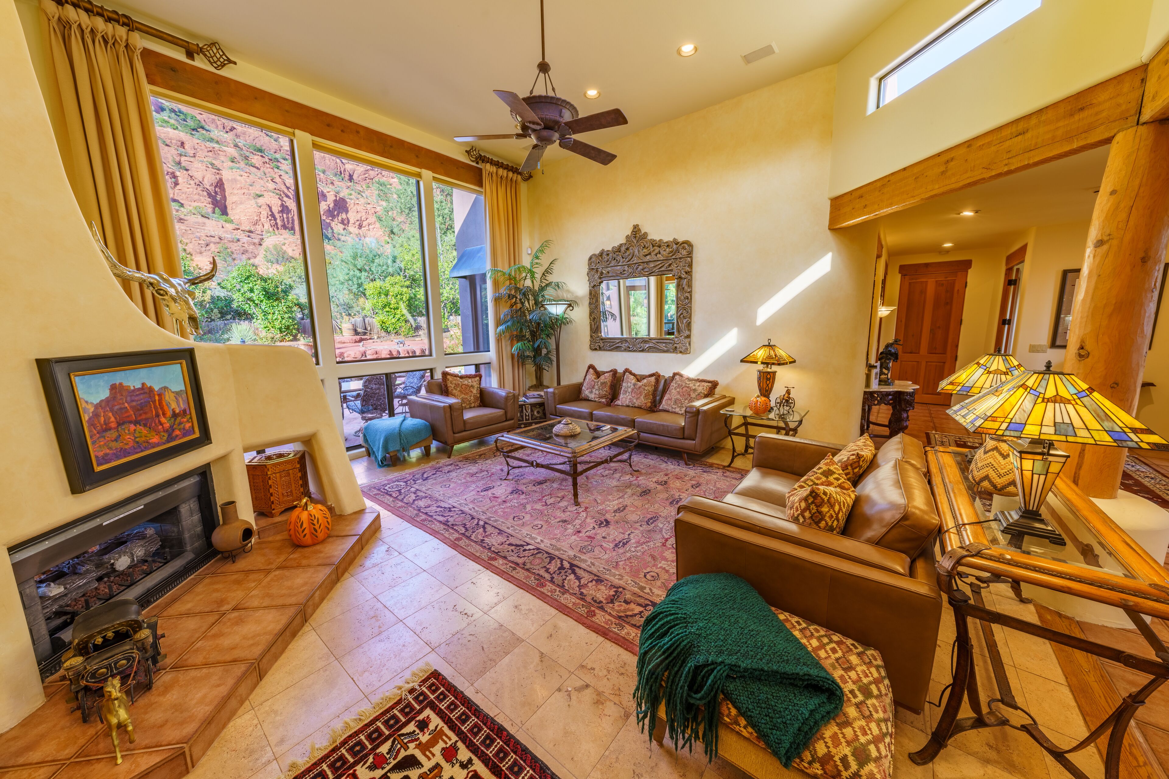 A spacious living room with a fireplace, large windows, and a ceiling fan.