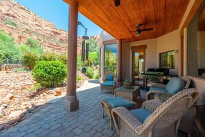 Un patio cubierto con mobiliario de mimbre, una parrilla y vistas a formaciones rocosas rojas.
