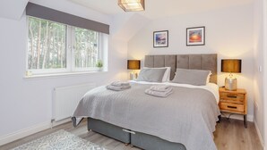 A bedroom with a large bed, two bedside lamps, a window with a view of trees, and a radiator. - 4 bedroom accommodation in Craigellachie (Craigellachie)
