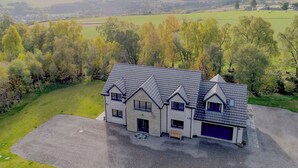 A large, modern house with a grey roof and multiple windows, surrounded by a well-maintained lawn and trees. - 4 bedroom accommodation in Craigellachie (Craigellachie)