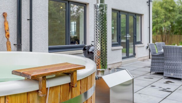A hot tub with a wooden deck, a metal grill, and a glass enclosure. - 4 bedroom accommodation in Craigellachie (Craigellachie)