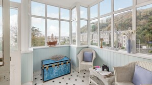A room with large bay windows, a blue trunk, wicker furniture, and a view of a town. - 2 bedroom accommodation in Barmouth (Barmouth)